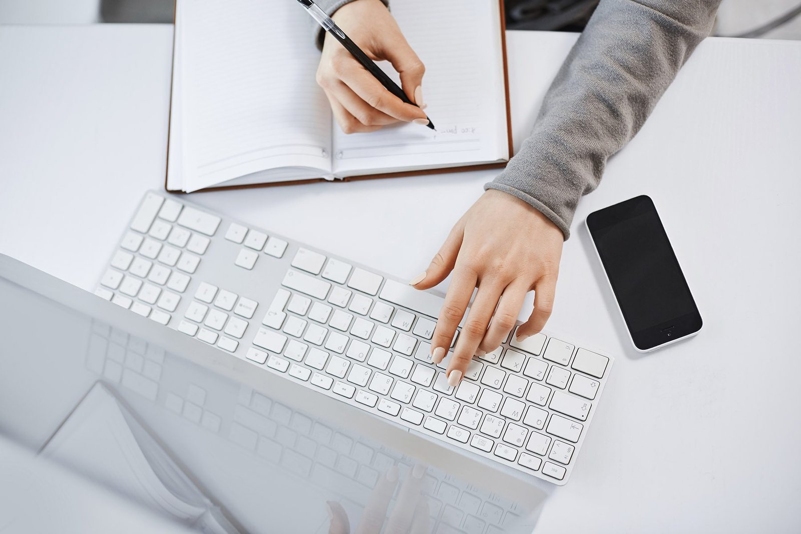 High angle shot of woman hands typing on keyboard. Focused female student working on her homework on computer, making notes, waiting for important call from boss and glancing at smartphone. Alt: Posiciono tu pagina lo mas alto en Google con seo